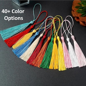 May include: A collection of colorful tassels in various shades, including teal, red, yellow, and pink. Each tassel has a looped cord for hanging. The image includes the text "40+ Color Options".