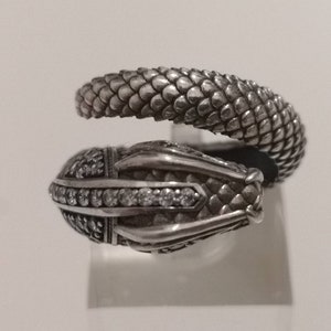 May include: A silver snake ring with a detailed, textured design and clear stones on the head.