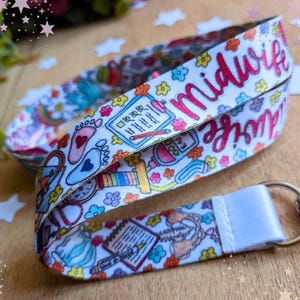 May include: A white fabric lanyard featuring a colorful repeating pattern of medical icons including baby footprints, clipboards, stethoscopes, and flowers. The word Midwife is printed in pink script. A silver metal swivel clasp is attached to the end.