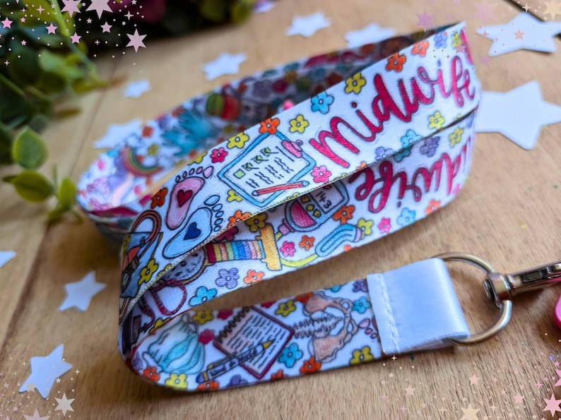May include: A white fabric lanyard featuring a colorful repeating pattern of medical icons including baby footprints, clipboards, stethoscopes, and flowers. The word Midwife is printed in pink script. A silver metal swivel clasp is attached to the end.