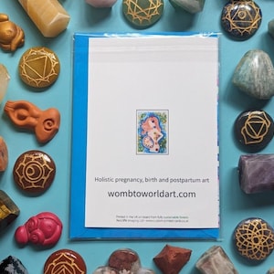 May include: A blue card with a white background and a colorful illustration of a woman with a flower crown. The text on the card reads "Holistic pregnancy, birth and postpartum art wombtoworldart.com".