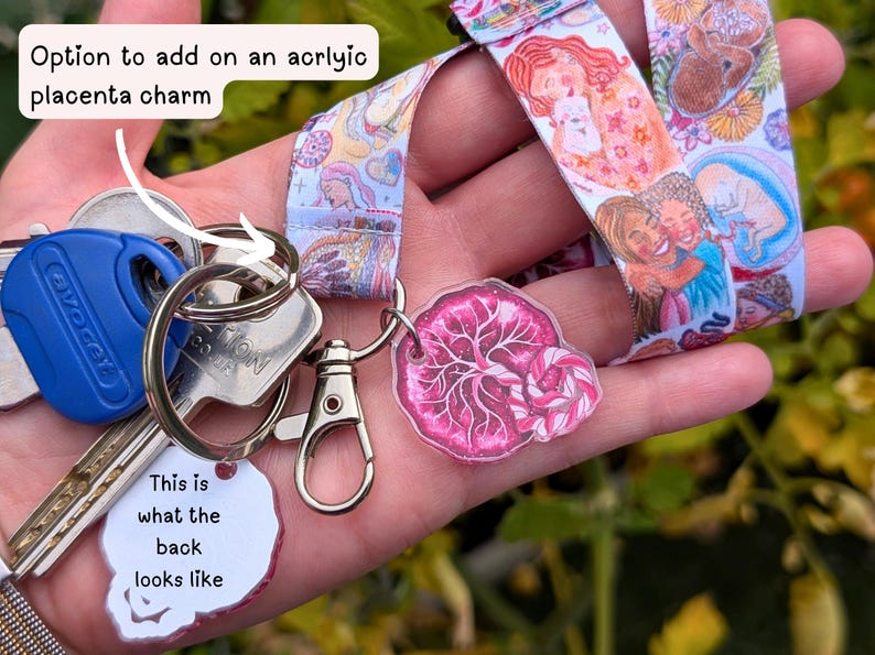 May include: A fabric lanyard featuring a colorful illustration of people and fetuses, attached to a metal keyring with a blue key and a pink acrylic placenta charm. The charm has a white back with the text: This is what the back looks like.