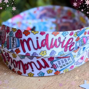May include: A white fabric lanyard featuring a repeating pattern of colorful flowers, medical icons, and the word Midwife written in a bold pink script. The design includes illustrations of a clipboard, a coffee cup, and baby footprints.