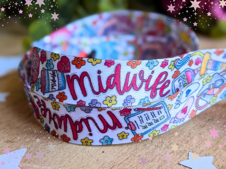 May include: A white fabric lanyard featuring a repeating pattern of colorful flowers, medical icons, and the word Midwife written in a bold pink script. The design includes illustrations of a clipboard, a coffee cup, and baby footprints.