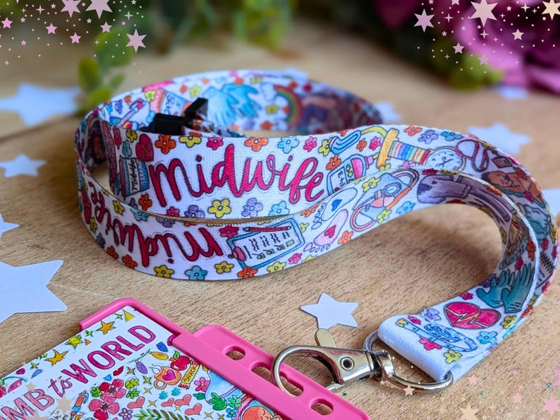 May include: A white fabric lanyard featuring a colorful repeating pattern of medical icons, flowers, and the word midwife in pink script. The lanyard includes a silver metal lobster clasp attached to a bright pink plastic ID badge holder.