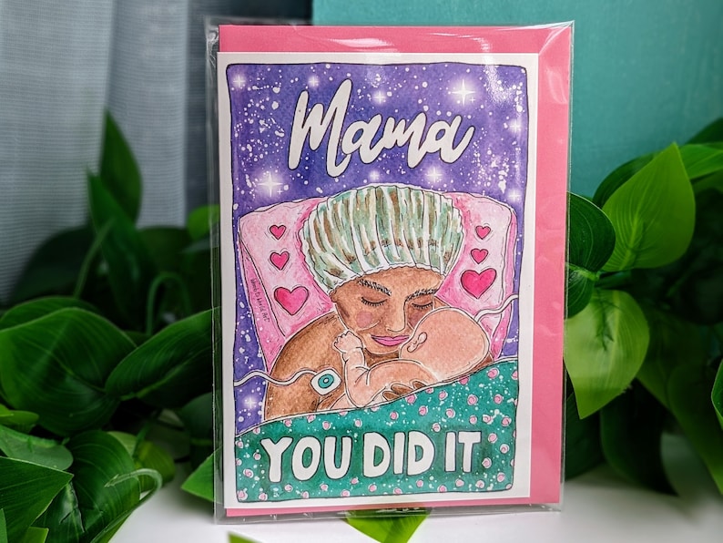 Op de afbeelding: Een roze kaart met een paarse en witte illustratie van een vrouw in een ziekenhuisbed die een baby vasthoudt. De vrouw draagt een chirurgische muts en de baby is gewikkeld. De tekst "Mama you did it." staat in groen en wit op de kaart.