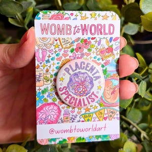 Puede incluir: Una tarjeta colorida con el texto "WOMB to WORLD" y un botón que dice "PLACENTA SPECIALIST". La tarjeta tiene un diseño caprichoso con flores, estrellas e ilustraciones relacionadas con bebés. El botón es redondo con un diseño de placenta morada.