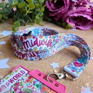 May include: A white fabric lanyard featuring a colorful repeating pattern of medical icons, flowers, and the word midwife in pink script. The lanyard includes a silver metal swivel lobster clasp attached to a bright pink plastic ID badge holder.