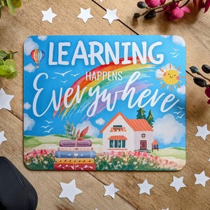 May include: A blue and green mouse mat with a rainbow, a house, and a stack of books. The text on the mouse mat reads "Learning Happens Everywhere."