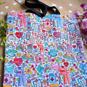 May include: A white tote bag with a colorful print of various medical and nursing-related items, including hearts, stethoscopes, bandages, pills, and rainbows. The text "Nurse" appears multiple times on the bag.
