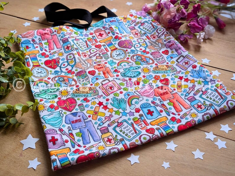 May include: A white tote bag with a colorful pattern of medical-themed illustrations. The pattern includes hearts, bandages, pills, syringes, stethoscopes, and the word "NURSE".