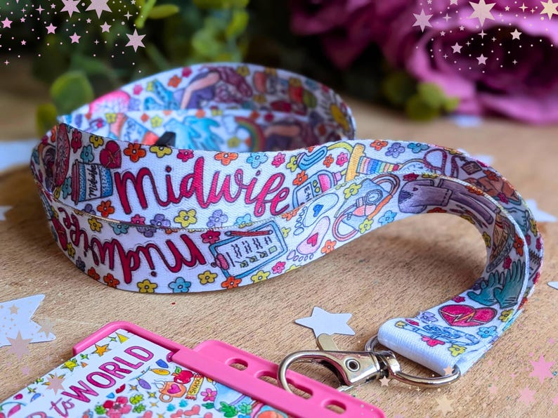 May include: A white fabric lanyard featuring a colorful repeating pattern of medical icons, flowers, and the word midwife in pink script. The lanyard includes a silver metal lobster clasp attached to a bright pink plastic badge holder.