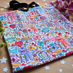 May include: A white tote bag with a colorful print of medical symbols, hearts, stars, and rainbows. The print includes the words "Nurse" and "Anatomy & Physiology".