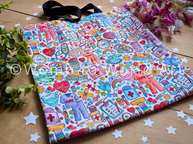 May include: A white tote bag with a colorful print of medical symbols, hearts, stars, and rainbows. The print includes the words "Nurse" and "Anatomy & Physiology".