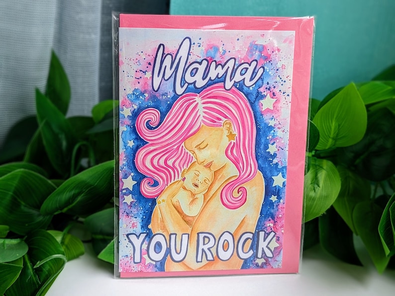 May include: A pink and blue watercolor card with a mother and child. The mother has pink hair and is holding the child. The card says "Mama You Rock" in white letters.