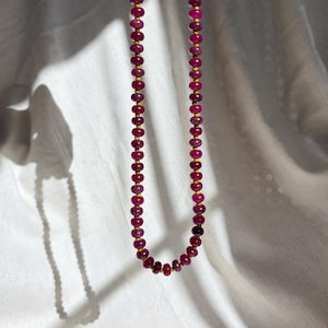 May include: A necklace featuring a single strand of small, round, deep magenta-colored beads separated by tiny, bright yellow spacers. The beads are uniform in size and shape, creating a continuous circular pattern along the length of the string.