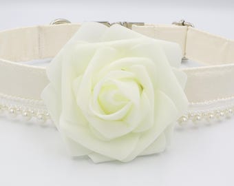 May include: Ivory-colored pet collar featuring a large, white rose accent. The collar has a pearl bead trim and a silver-tone metal clasp. The collar is made of a soft, fabric material.