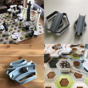 Pu&ograve; includere: Un gioco di percorso per biglie con una variet&agrave; di binari e torri in plastica grigia. Il gioco &egrave; impostato su una scacchiera esagonale bianca con uno sfondo verde. Ci sono diverse biglie in una ciotola di plastica grigia.