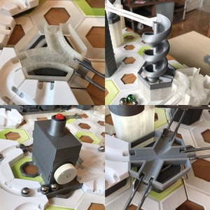 Pu&ograve; includere: Primo piano di un gioco di biglie con vari pezzi di pista, tra cui una spirale, un interruttore e una pista curva. I pezzi della pista sono in plastica bianca e grigia. Ci sono anche diverse piccole biglie metalliche sulla pista.