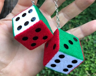 May include: A pair of fuzzy dice, each with a red and green color scheme, connected by a silver chain. The dice have white faces with black dots. The dice are held up against a green background.