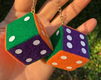 Op de afbeelding: Twee pluche dobbelstenen die aan een gouden ketting hangen. De dobbelstenen zijn groen, paars en oranje met witte stippen.