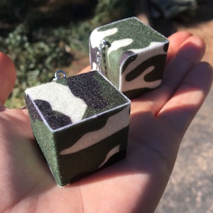 May include: Two small, green, white, and black camouflage cube-shaped keychains with silver chains.