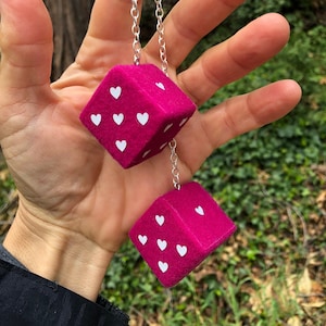 May include: Two pink fuzzy dice with white hearts hanging from a silver chain.