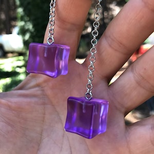 May include: A silver chain necklace with two dangling purple square charms. The charms are translucent and have a slight shimmer.