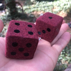 May include: Two red felt dice with black dots. The dice are hanging from a silver chain.