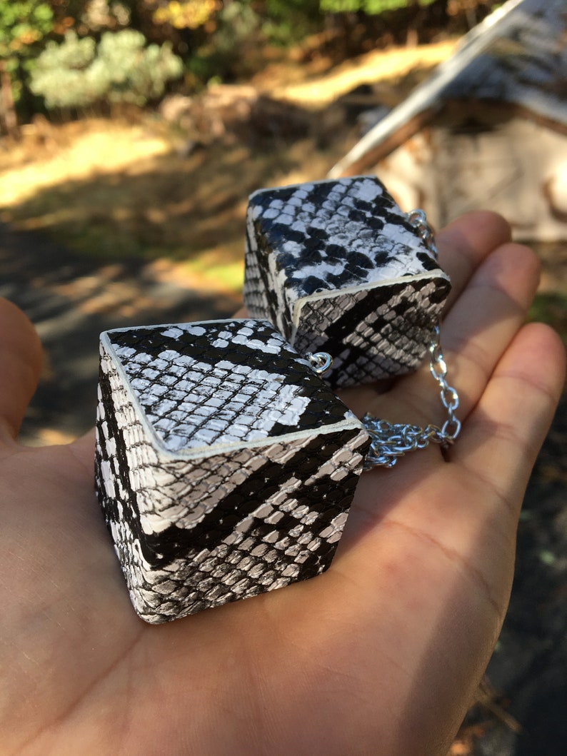 Pu&ograve; includere: Due cubi con motivo a pelle di serpente in bianco e nero collegati da una catena argentata.