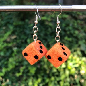 May include: A pair of orange felt dice earrings with black dots. The dice are hanging from silver chains and hooks.