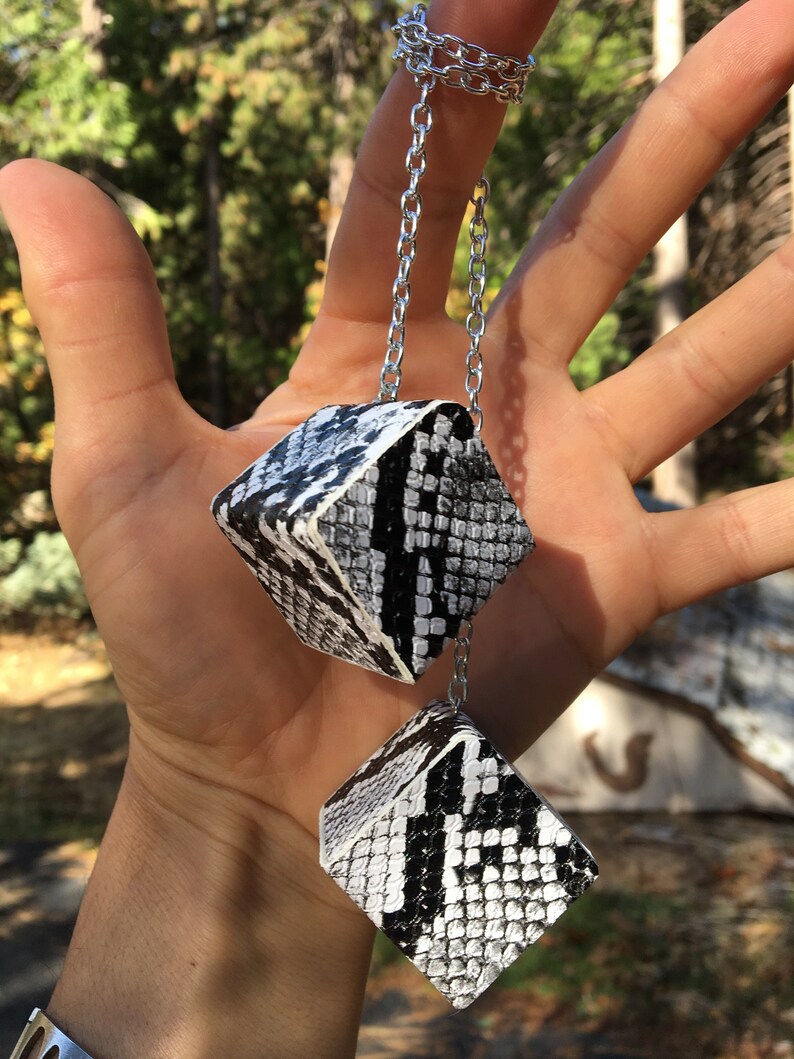 Pu&ograve; includere: Una collana con catena d'argento con due ciondoli a forma di cubo con motivo a pelle di serpente bianco e nero.