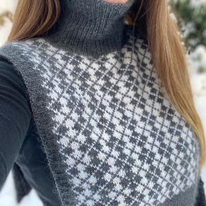 May include: A gray and white knitted cowl and vest set. The vest features a houndstooth pattern in gray and white. The cowl is a solid gray color. The set is made of a soft, textured yarn.