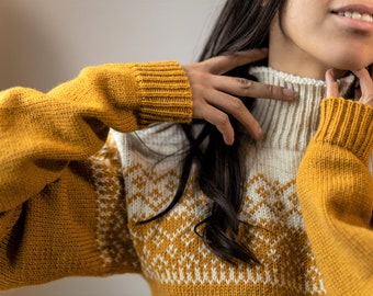 Puede incluir: Primer plano de una mujer con un suéter de punto amarillo y blanco con un patrón de punto de trenza. El suéter tiene cuello alto y mangas largas.