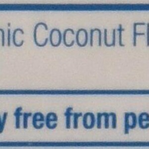 Puede incluir: Una etiqueta azul y blanca con el texto "Ingredientes: Harina de coco org&aacute;nica" y "Contiene: Coco". La etiqueta tambi&eacute;n indica "Procesado en una instalaci&oacute;n libre de cacahuetes, soja y OMG".
