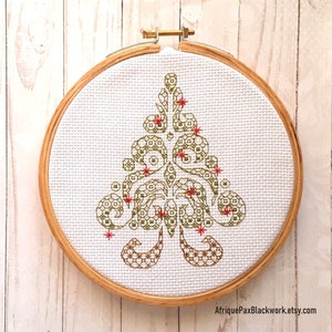 May include: A green and red embroidered Christmas tree design in a wooden embroidery hoop. The design features a stylized tree with geometric patterns and red stars.
