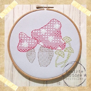 May include: A white embroidery hoop with a cross-stitch design of red and green mushrooms. The hoop is labelled "Prairie Bridge Stitchery".