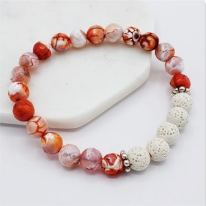 May include: A bracelet made with orange and white agate beads and white lava rock beads. The bracelet has a silver accent between the agate and lava rock beads.