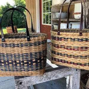 May include: Two woven baskets with leather handles. The basket on the left has a blue and black geometric pattern. The basket on the right has a red, blue, and black striped pattern.