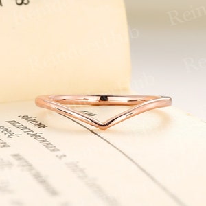 May include: A rose gold V-shaped wedding band. The band is thin and delicate, and it is made of a smooth metal.