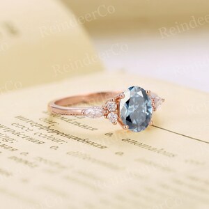 May include: A rose gold engagement ring with a large oval-shaped blue gemstone surrounded by smaller diamonds. The ring is set on a white background.