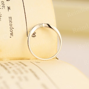 K&ouml;nnte beinhalten: Ein zarter Ring aus Wei&szlig;gold mit einem kleinen Diamanten in der Mitte. Der Ring liegt auf einer cremefarbenen Oberfl&auml;che.