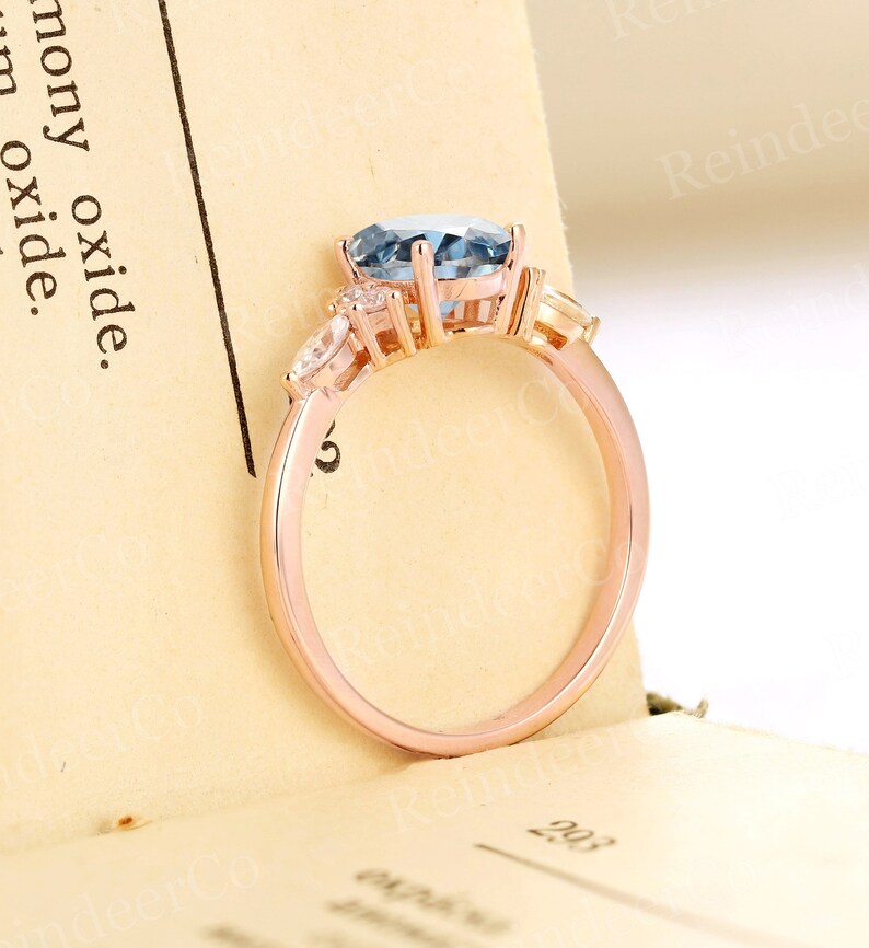 May include: A rose gold engagement ring with a blue oval-shaped center stone and two smaller pear-shaped stones on either side.
