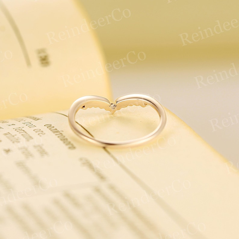 K&ouml;nnte beinhalten: Ein goldener Ring mit einem kleinen Diamanten in der Mitte und zwei Fl&uuml;geln auf jeder Seite. Der Ring liegt auf einer wei&szlig;en Oberfl&auml;che.