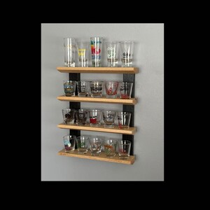 Op de afbeelding: Een houten shotglazen displayrek met zwarte metalen beugels. Het rek heeft vier niveaus en is gevuld met shotglazen. De shotglazen zijn van helder glas met verschillende ontwerpen en logo's.