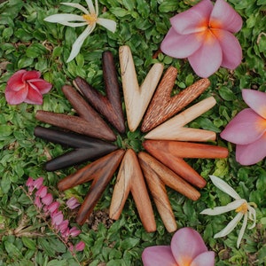 May include: A set of 12 wooden V-shaped tools arranged in a circle on a bed of green grass and pink flowers. The tools are made of different types of wood and have a natural finish.