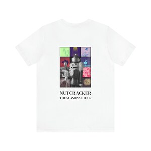 May include: White t-shirt with a black and white image of a Nutcracker doll surrounded by colorful squares. The text "NUTCRACKER THE SEASONAL TOUR" is printed below the image.