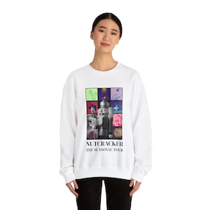 May include: White sweatshirt with a colorful collage of images featuring a Nutcracker doll. The text "Nutcracker The Seasonal Tour" is printed below the collage.
