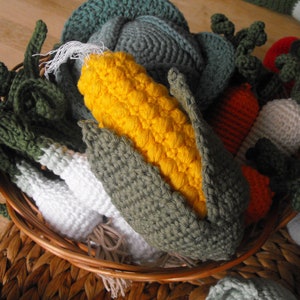 Könnte beinhalten: Ein Korb gefüllt mit gehäkelten Gemüse, darunter eine grüne Zwiebel, eine weiße Rübe, ein grüner Kohl, eine rote Paprika, ein gelber Maiskolben und eine grüne Bohne.