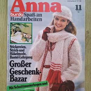 Może przedstawiać: Wydanie magazynu Anna Burda z listopada 1981 roku z okładką przedstawiającą osobę w puszystym, jasnoróżowym swetrze z dzianiny, pasującej czapce i szaliku z czerwonymi akcentami, trzymającą brązową okrągłą torebkę.